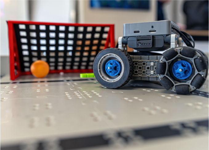 Close-up of a wheeled robot on a competition field with a goal net and ball